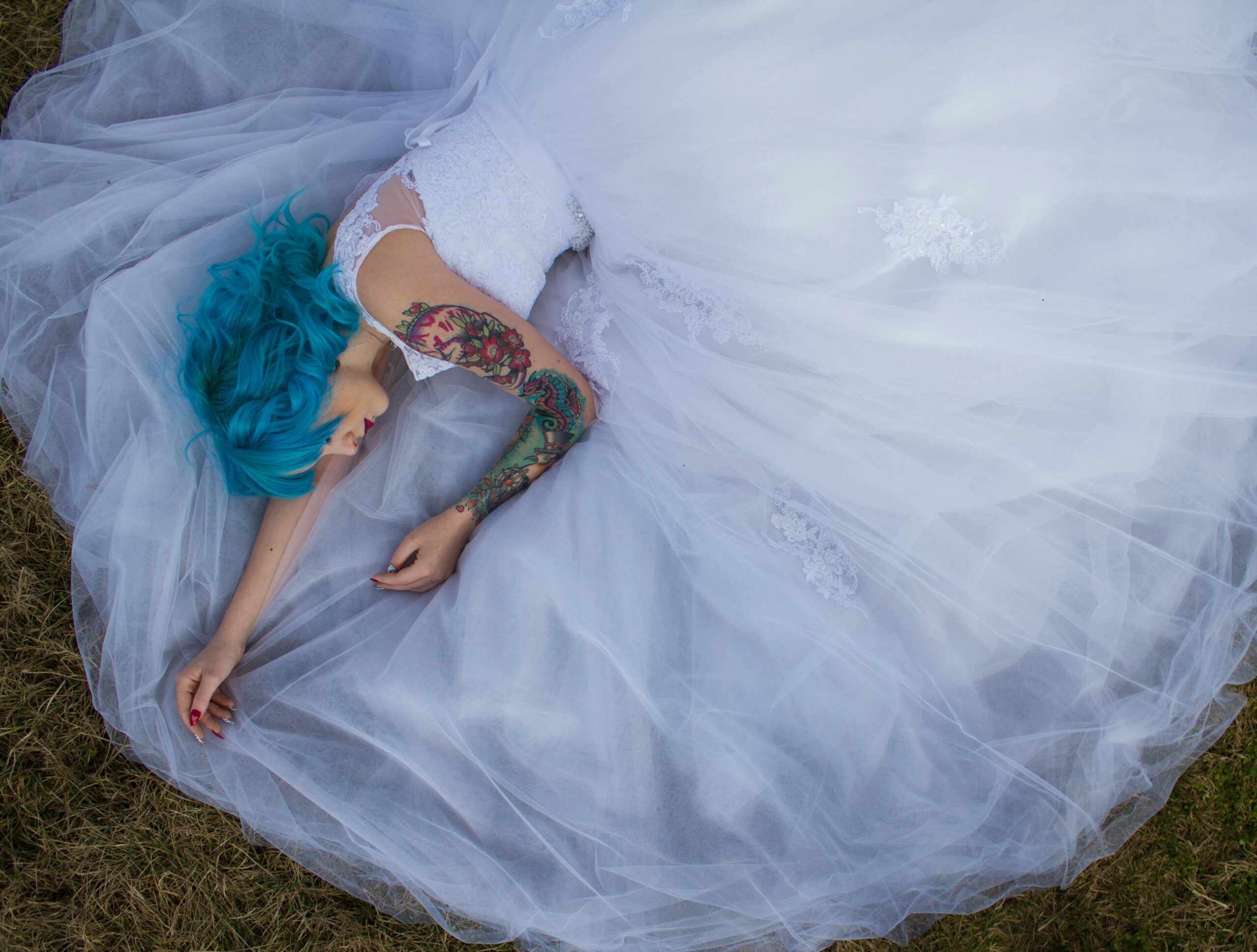 Captivating image of a bride with blue hair and tattoos in a white wedding dress outdoors.